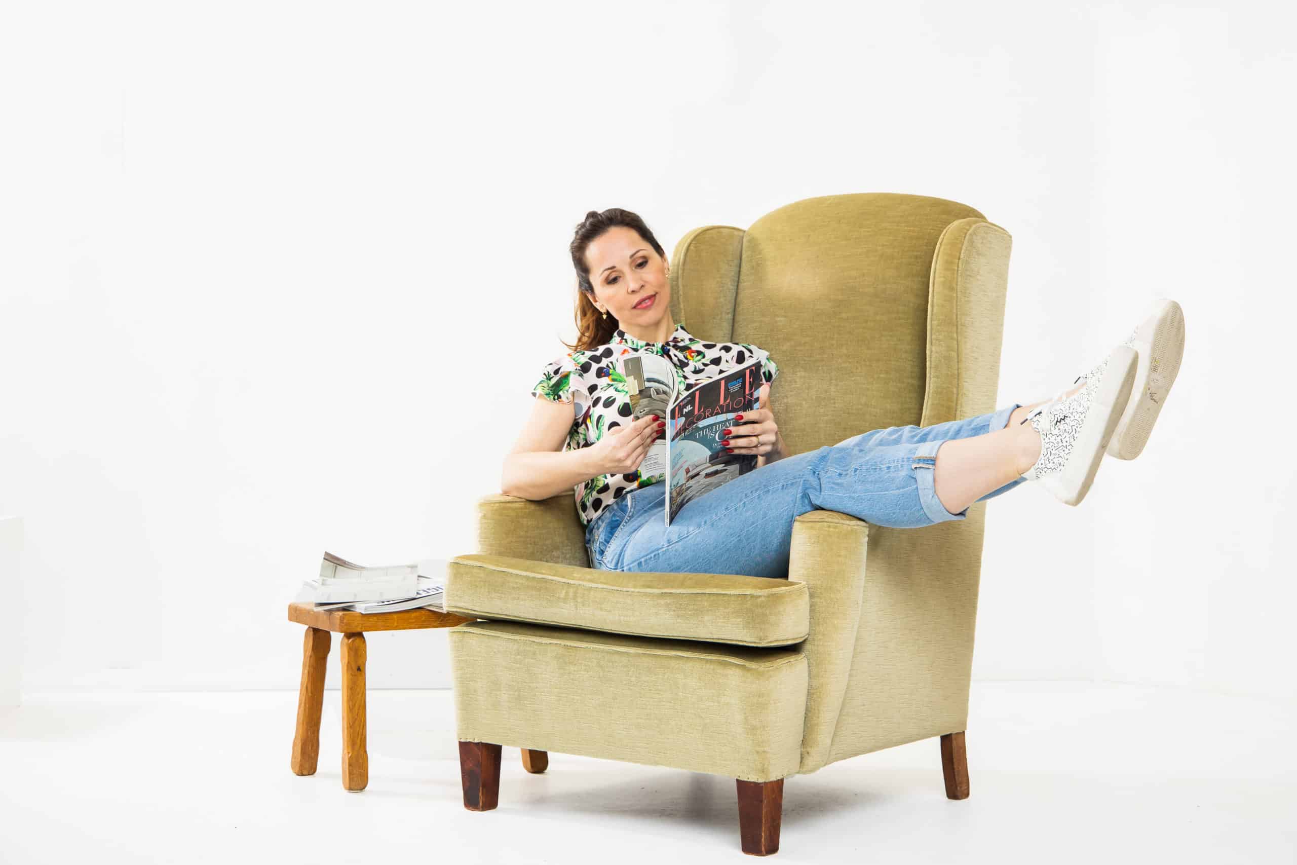 martina fens eigenaar van aangenaam interieuradvies zit op een stoel en leest een interieurmagazine